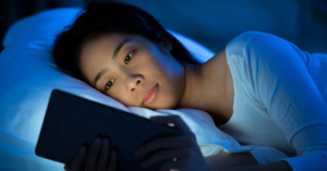 Woman using tablet in bed at night, showing how blue light and melatonin suppression can affect sleep