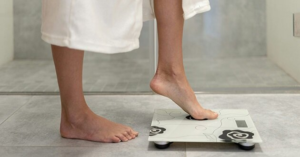Woman stepping on scale at home, illustrating how poor sleep can cause weight gain and affect metabolism.