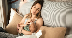 Exhausted mother holding baby in bed, illustrating hormonal sleep disruption