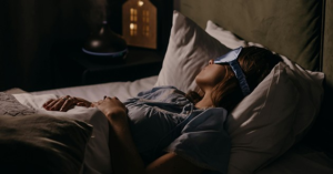 Woman sleeping in bed wearing a blue sleep mask, illustrating tips on how to fall asleep faster in a calm bedroom setting.