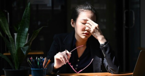 ed woman at desk holding her head, showing poor sleep quality signs