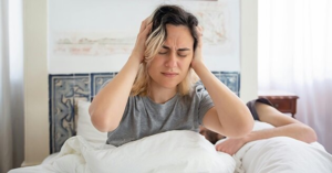 Woman in bed holding her head, waking up with a headache likely due to hormonal morning headaches