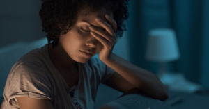 Woman awake at night with hand on forehead, possibly waking up at 3am due to cortisol spikes